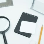 Home A magnifying glass, notebook, and pencil on a pale desk